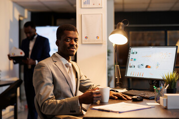 Fototapeta premium Businessman standing at desk table analyzing company statistics, working at financial growth report before start preparing investment strategy. Entrepreneur working late at night in startup office