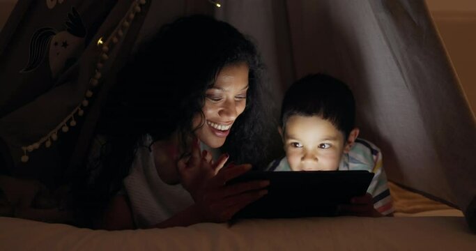 Bed, night and mother with boy, tablet and cheerful with fun and playing on a weekend break. Parent, family and mama with son and technology with digital app and home with smile and goofy with joy