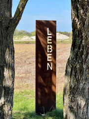 Metal stele with the inscription "Leben" (means: Life) between two old trees at the edge of a field