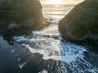 Waves crashing in an inlet at sunset. Bethells Beach, Auckland, New Zealand.