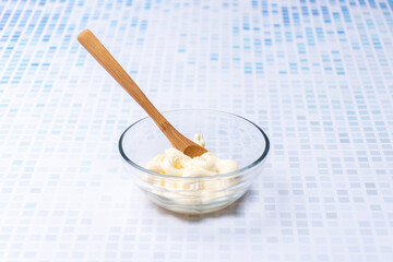 Glass bowl with mayonnaise and a wooden spoon.