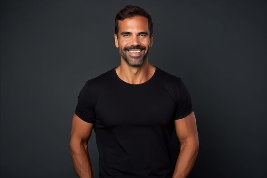Handsome man in black t-shirt smiling at camera while standing against grey background