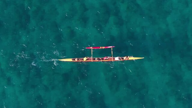 Overhead view on athletic people boating the traditional Hawaiian Canoe on Oahu. Water activity shot in scenic clear blue green ocean waters 4K. Top down shot of sports team sailing in outrigger canoe
