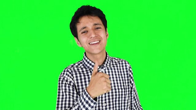 Joven hombre caucasico con camisa a cuadros sonr&iacute;e y hace gesto de aprobaci&oacute;n o like con su pulgar arriba sobre un fondo verde