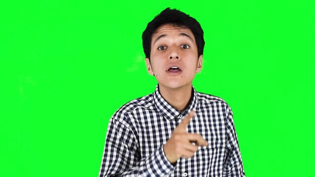 Joven hombre negando diciendo que no y callando con el dedo sobre un fondo verde