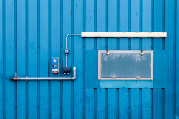 Industrial abstract blue corrugated metal wall with pipes, wires and dials