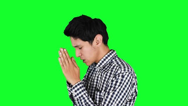 Joven hombre delgado caucasico orando sobre un fondo verde aislado