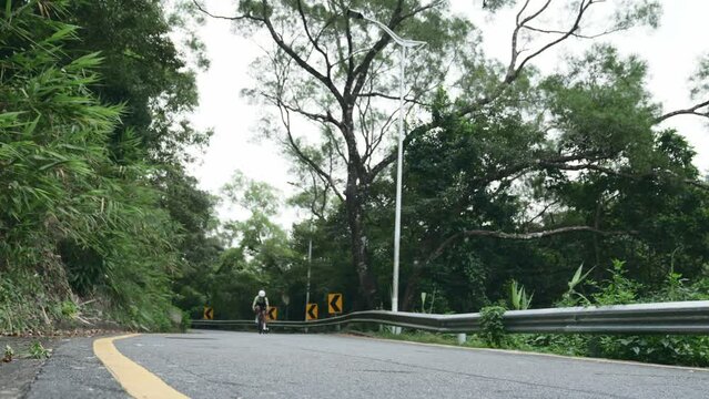 young asian female cycling athlete riding bike on rural road