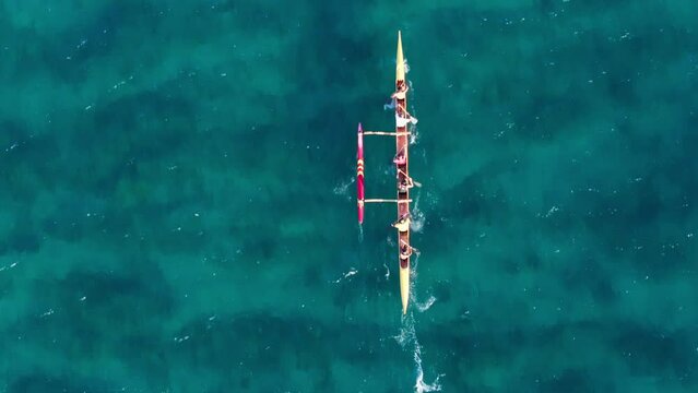 Top down shot of sports team sailing in outrigger canoe. Overhead view on athletic people boating the traditional Hawaiian Canoe on Oahu. Water activity shot in scenic clear blue green ocean waters 4K