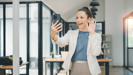 Business woman concept, Professional woman in office attire using smartphone for a friendly video call, waving hello.