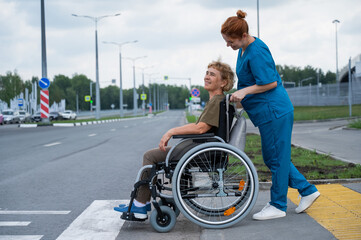 Red-haired nurse pushing an elderly woman in a wheelchair across the road. 