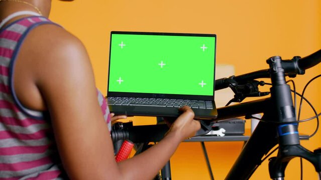 Mechanic doing bike servicing in studio background atelier shop, looking on green screen laptop maintenance list. Specialist checking online for replacement bicycle parts on chroma key notebook