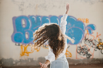 Stylish young woman with curly hair posing against the background of a graffiti wall.
