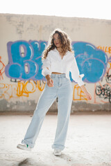 Stylish young woman with curly hair posing against the background of a graffiti wall.