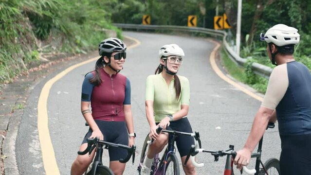 happy young asian cyclists chatting at roadside while take a break resting during outdoor riding