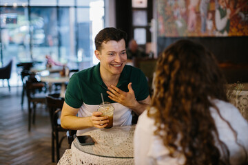 Happy young couple talking over a cup of coffee in a cafe, man and woman in a coffee shop on a date. - obrazy, fototapety, plakaty