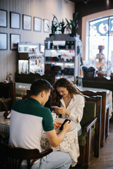 Cheerful young couple having a cup of coffee in a cafe, sending each other messages on the phone.