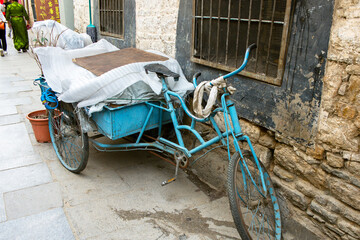 A weathered tricycle is parked next to a stone wall in Barkhor Square.
