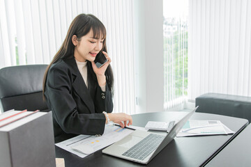 woman talking on the mobile phone and smiling while sitting at her working place in office.