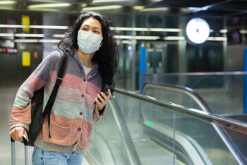 Asian woman in face mask with backpack walking in subway beside escolator