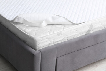 New soft mattress with protector on grey bed indoors, closeup