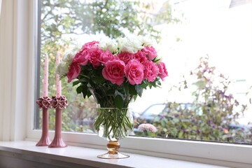 Vase with beautiful bouquet of roses and candles on windowsill indoors