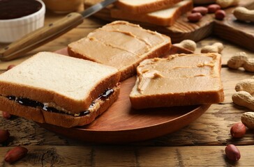Tasty peanut butter sandwiches with jam and peanuts on wooden table, closeup