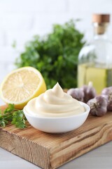 Obraz na płótnie Canvas Tasty mayonnaise sauce in bowl, parsley, garlic and lemon on white wooden table