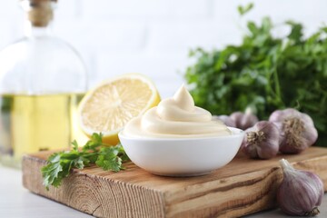 Obraz na płótnie Canvas Tasty mayonnaise sauce in bowl, parsley, garlic and lemon on table, closeup
