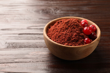 Dried cranberry powder and fresh berries in bowl on wooden table, closeup. Space for text