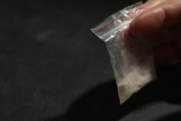 Addicted man with plastic bag of hard drug at grey table, closeup. Space for text