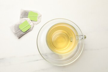 Tea bags and glass cup of hot beverage on white table, flat lay
