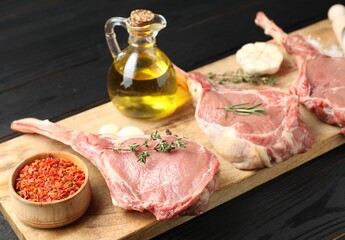 Fresh tomahawk beef cuts, spices and oil on black wooden table
