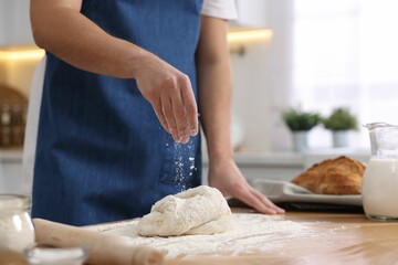 Obraz na płótnie Canvas Making bread. Man sprinkling flour onto dough at wooden table in kitchen, closeup