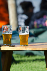 Two pints of lager sipping on outdoor bar table.
