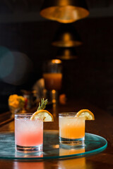 Pink and orange cocktails sitting on bar with a slight reflection and light flare