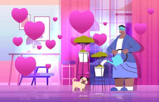elderly woman in love using watering can senior housewife taking care of house plants living room interior with pink hearts