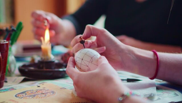Closeup on Artists Hands Drawing Traditional Ornate Designs on Easter Eggs with Stylus