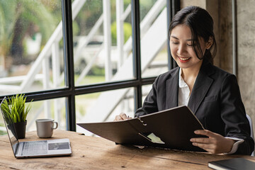 Cheerful Asian woman working with laptop in office, happy in formal suit working in office Charming smiling female office worker, financial accounting concept - obrazy, fototapety, plakaty