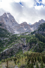A Waterfall on The Side of a Mountain Peak with Clouds and Snow Above Treeline in the Grand Teton National Park