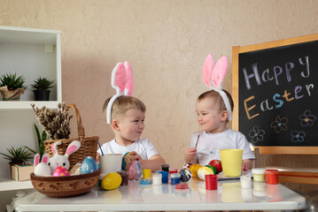 Two smiling children with bunny ears painting Easter eggs at home. Happy Easter concept