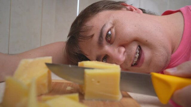 Portrait of obsessed man cutting pieces of hard cheese on wooden cutting board, looking with eyes of maniac Protein addiction healthy diet, fractional meals Hungry man preparing food Ravenous appetite