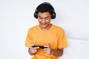 Asian teenage gamer boy wearing headphones and playing games online on smartphone © Queenmoonlite Studio