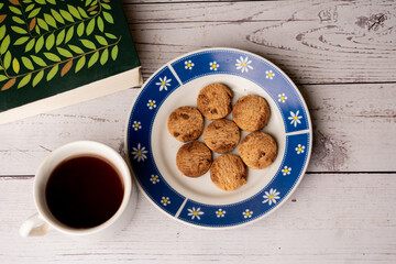 top view of a breakfast consisting of: chocolate chip cookies and a cup of hot chocolate and a book, on white wooden table