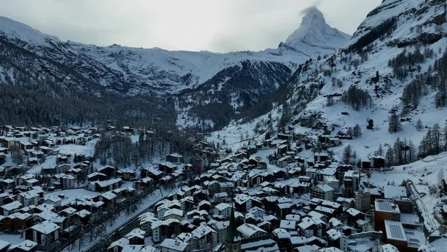 Zermatt ski resort and town with the matterhorn and houses in the back ground on a cloudy winter day in the Swiss Alps mountains. Aerial Drone Video