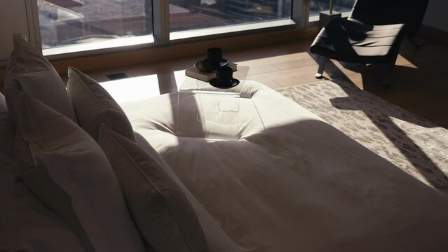 sun shades rising to reveal a bed with white bedding and a bedside tray that includes 2 coffee mugs and a book in a luxury bedroom