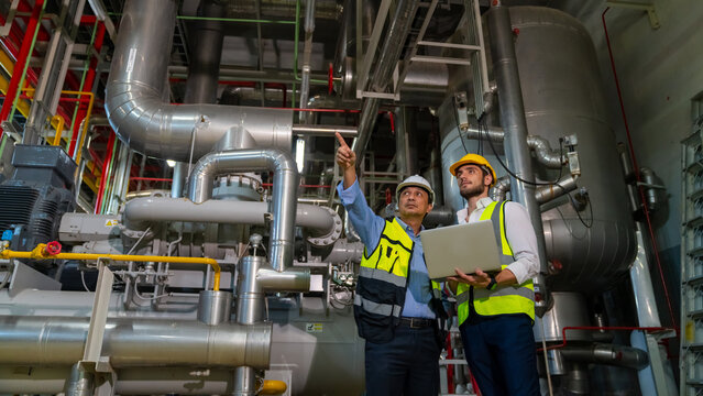 Professional male electrical engineer in safety uniform working and discussion at factory site control room. Industrial technician worker maintenance power system at manufacturing industry plant room.