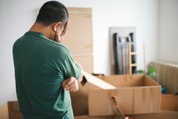 Back view of tired Man standing while looking at the cardboard boxes at home, preparation for...