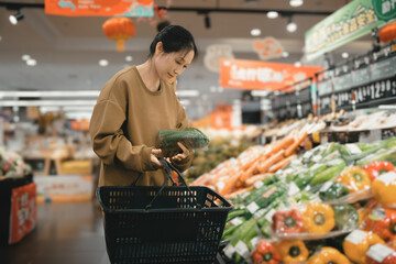 Asian women's portable shopping boxes choose fresh vegetables on the aisle of the supermarket...