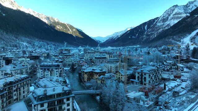 Low drone flyover of a river and ski village of Chamonix, France in the Alps mountain range on a cold winter morning with snow and Ice.